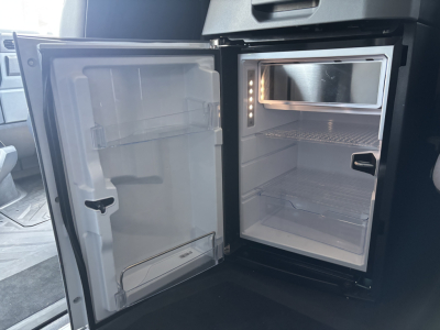 Truck interior showing open mini refrigerator/freezer unit in sleeper cab with empty shelves and door shelves.