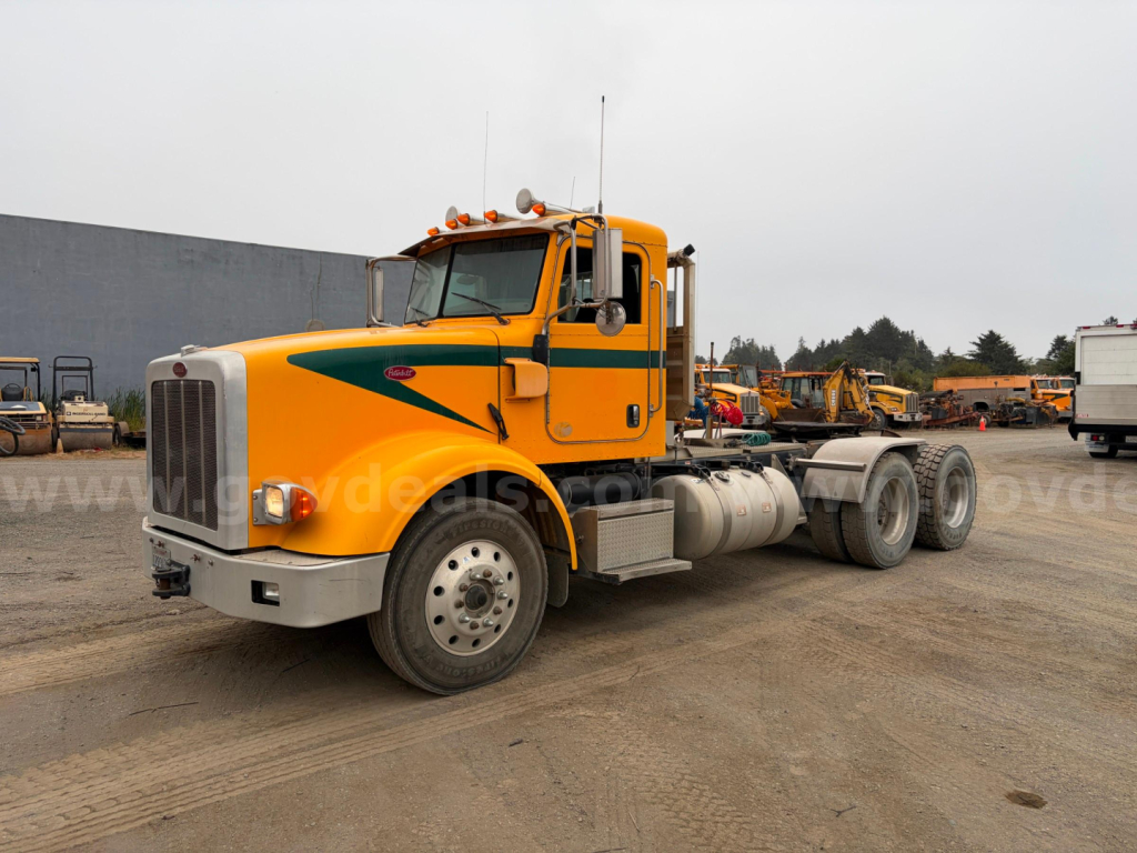 Peterbilt 367 heavy duty truck cab in yellow with green accent, front view, on dirt yard.