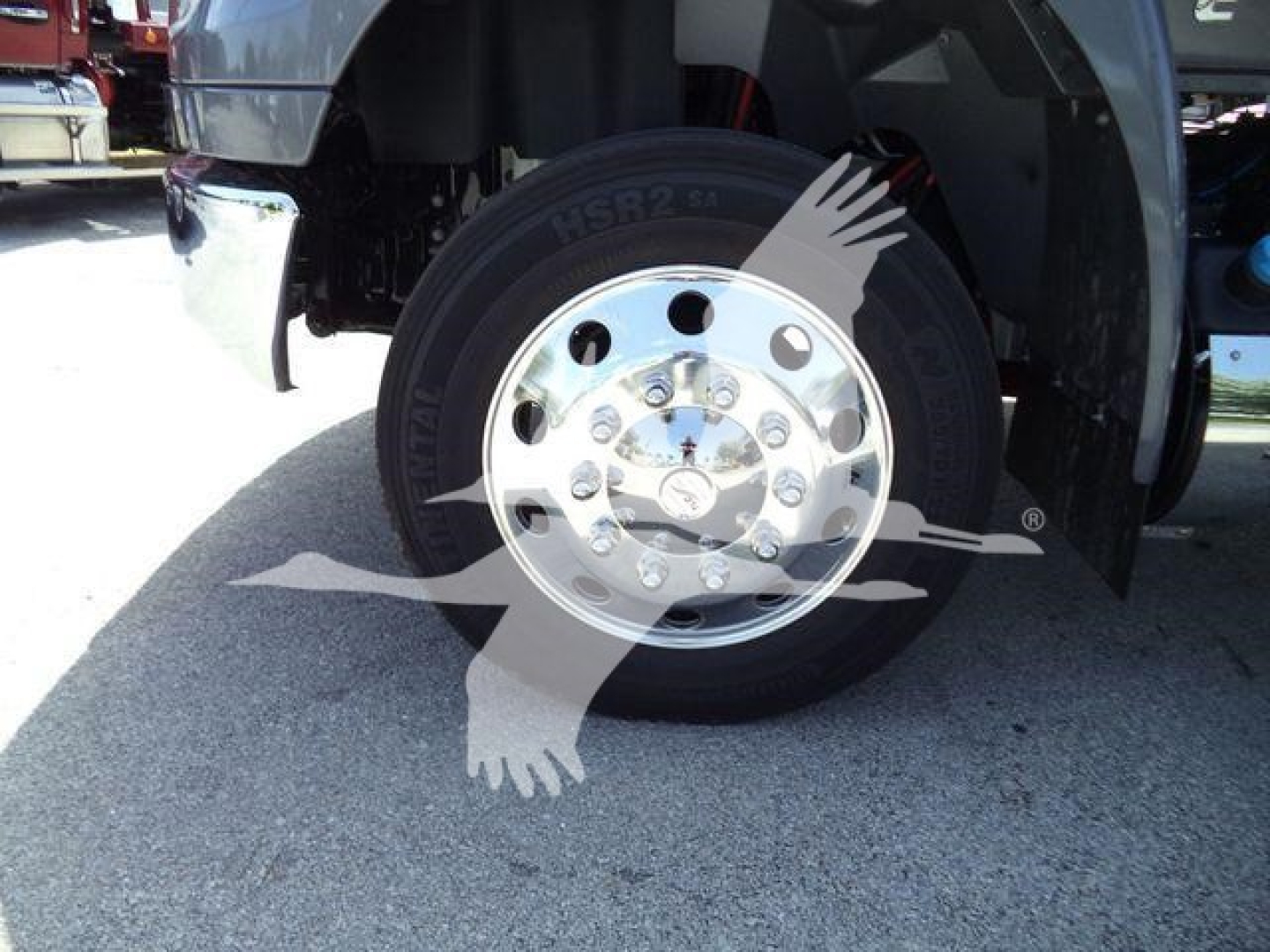 Truck front wheel showing chrome hubcap and tire with visible lug nuts; part of the wheel well and fender of a new International MV rollback truck.