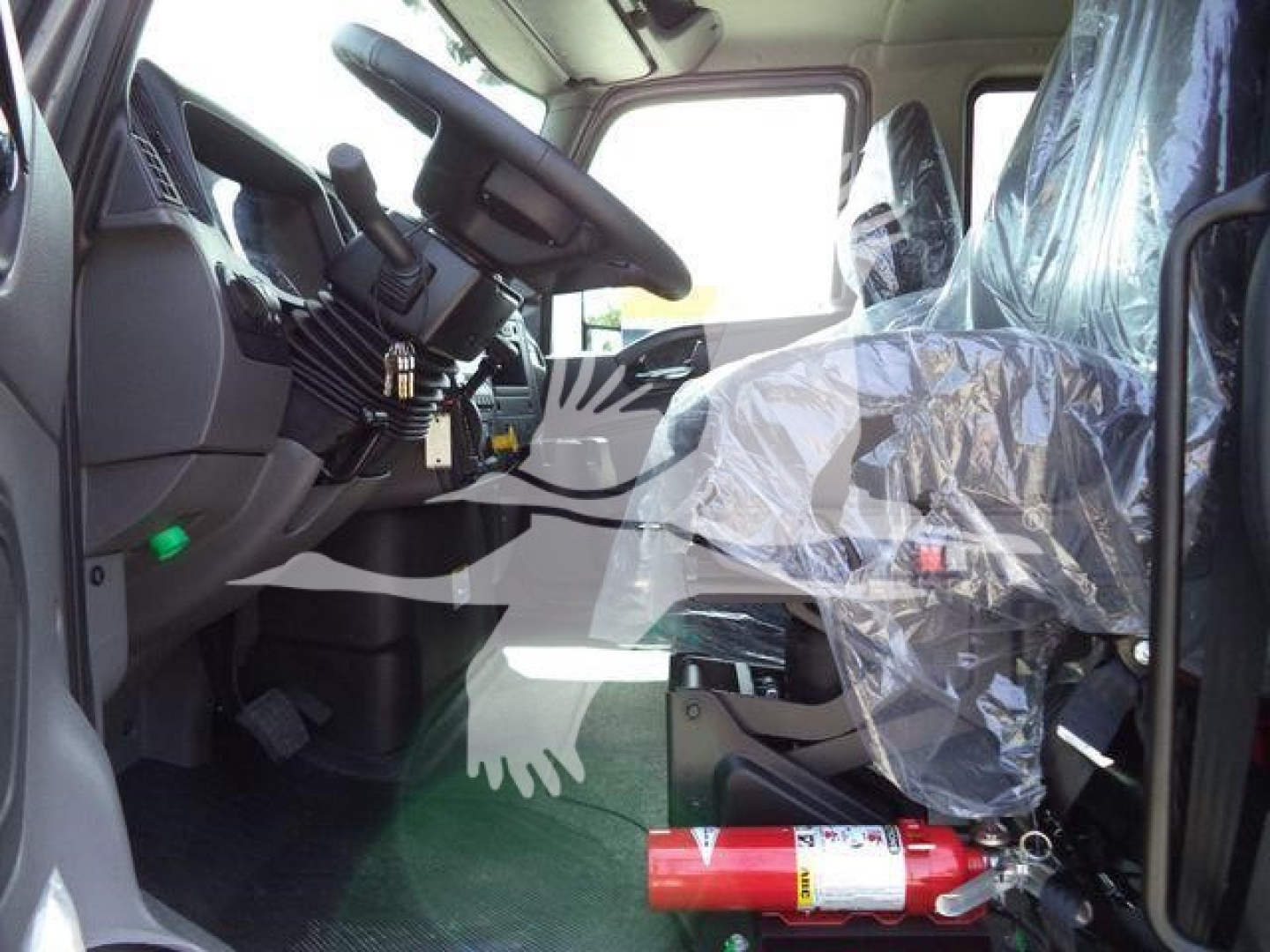 Cab interior of a 2027 International MV truck showing steering wheel, dashboard, pedals, and front passenger seat covered in plastic.