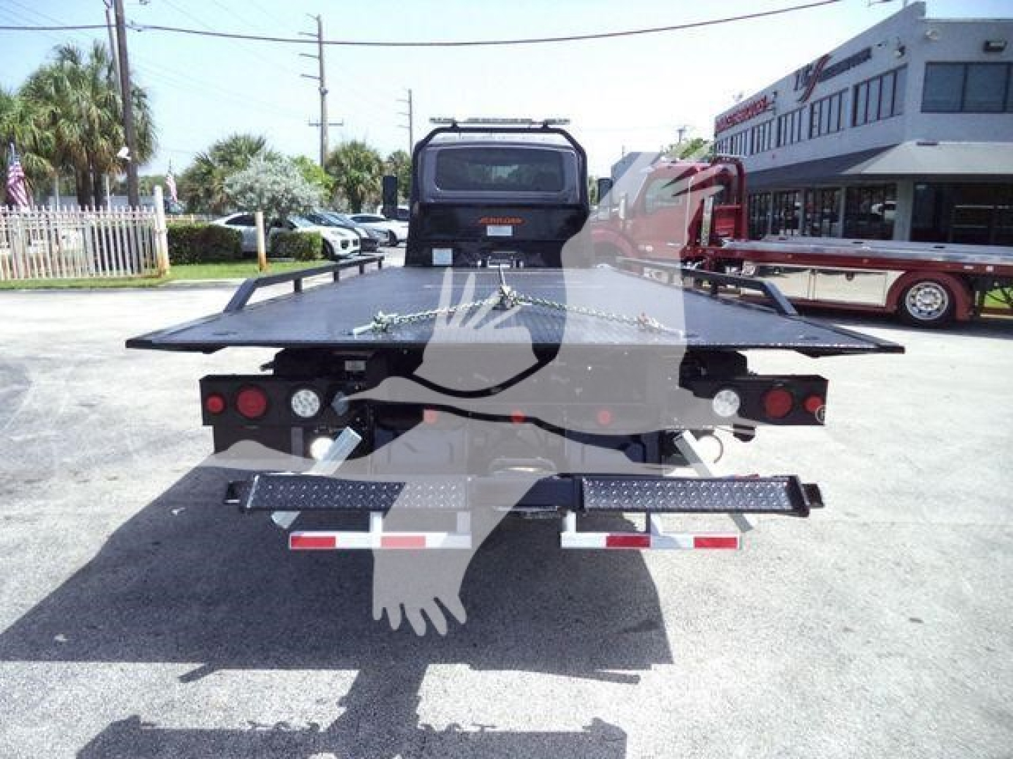 Back view of a new International MV rollback tow truck with flatbed, dual rear lights, and metal steps on each side.