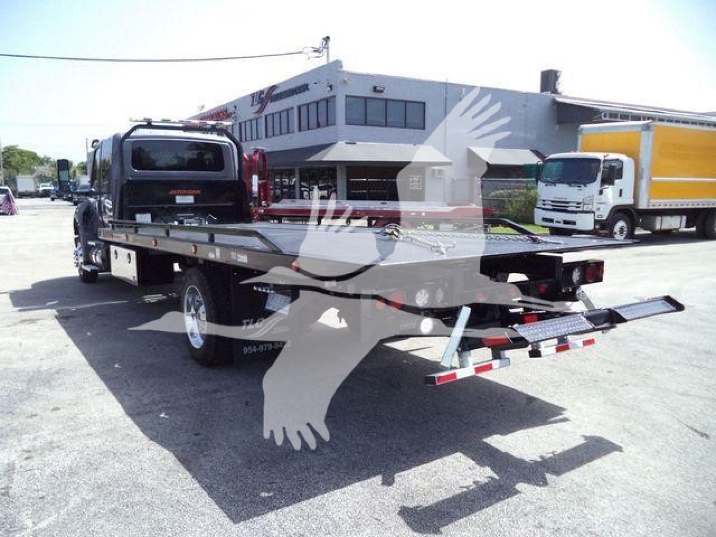 Tow truck rollback flatbed with black cab and rear loading ramps in a dealership lot.