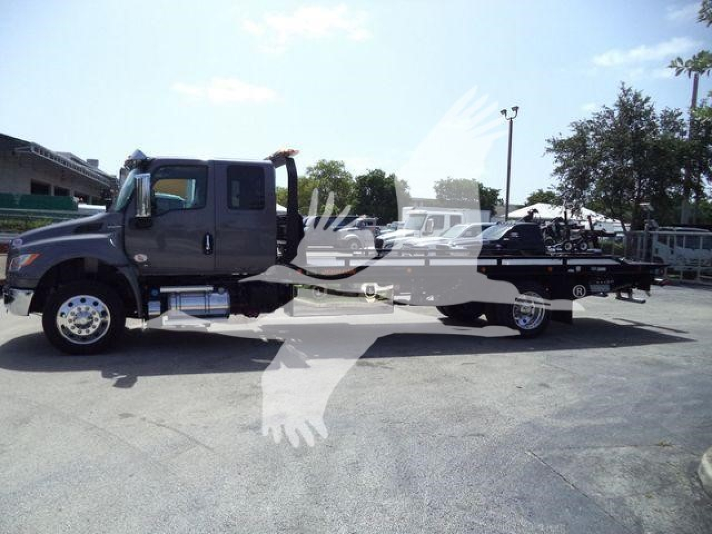 International MV rollback tow truck with long wheelbase and tow bed, side view showing cab and flatbed equipment, VIN 1HTEUMML0VS478861 windowed.