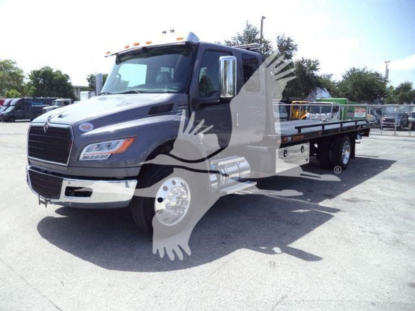 International MV rollback truck in a parking lot with flatbed, front grille, and side mirrors visible.