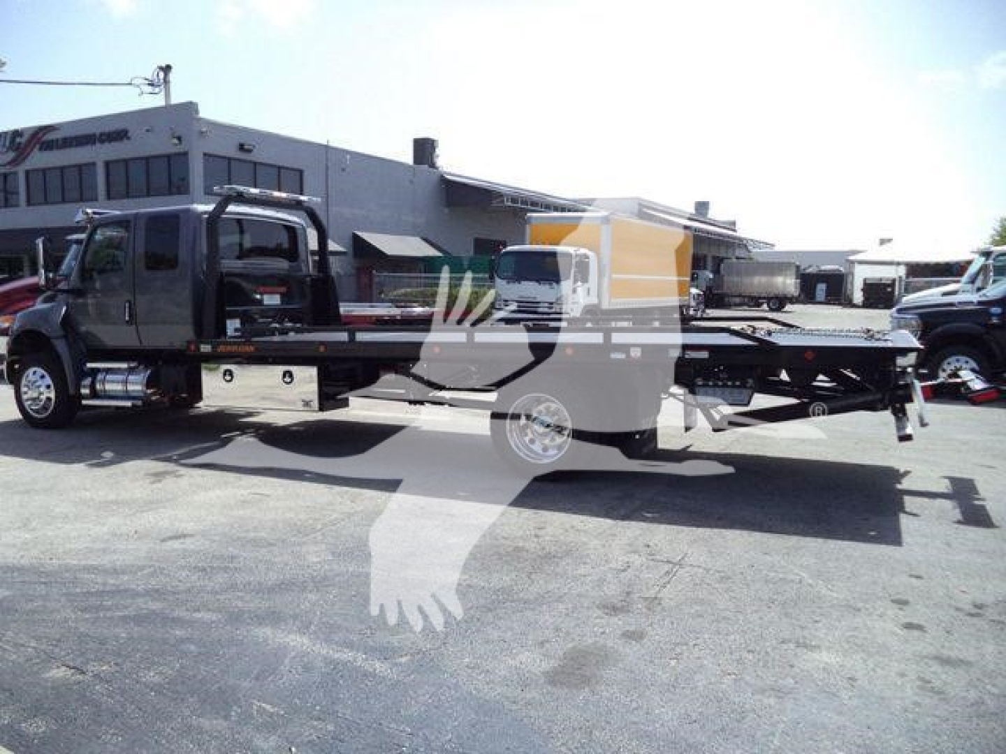 International MV rollback truck showing a flatbed wrecker in a dealership lot with other trucks in background.