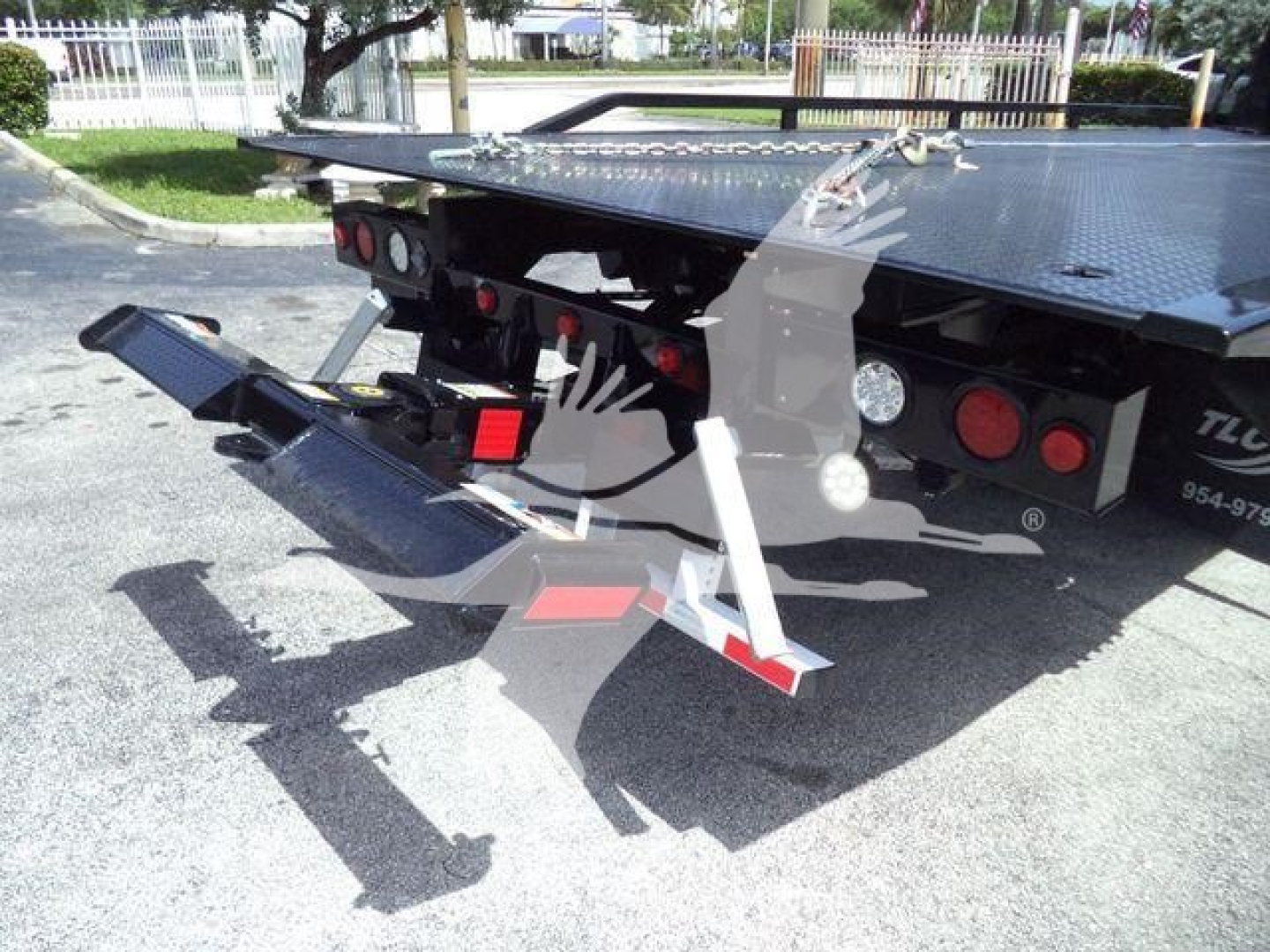 Towable rollback flatbed truck showing rear loading ramps and hydraulic components.