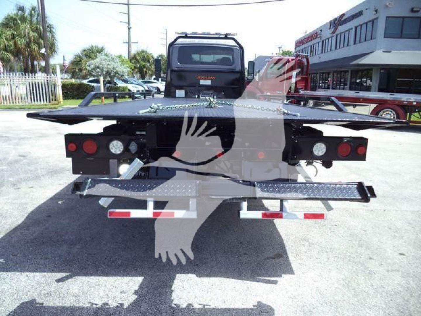 Truck rollback bed rear view with platform and taillights, VIN plate area not visible, dealership building in background.