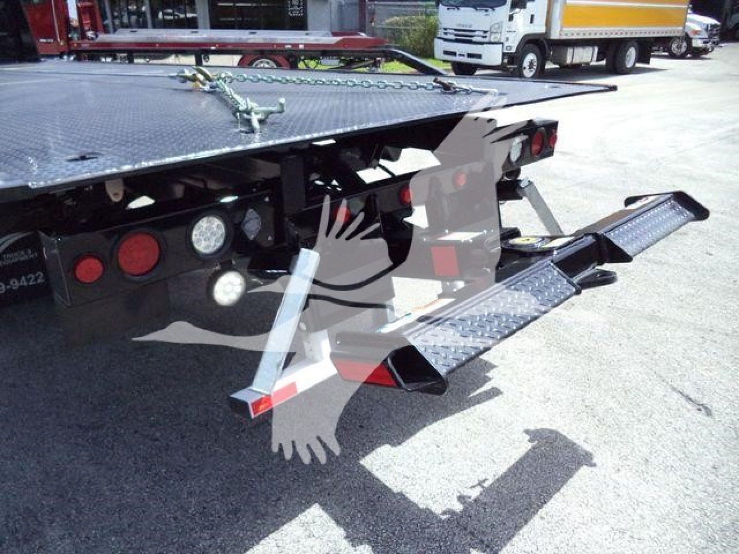 Back of rollback truck showing hydraulic ramps and lights; there are step plates and extension ramps with textured metal surface. Text visible near rear: none legible; general hardware components of tow truck bed.