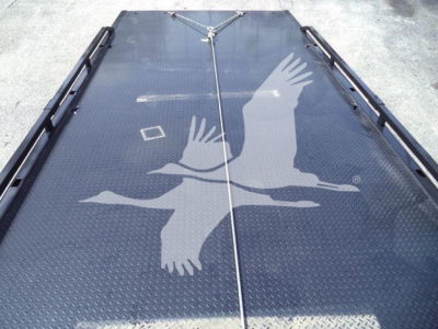 Flatbed trailer deck with engraved eagle graphic and chain tie-downs in center showing diamond plate surface.