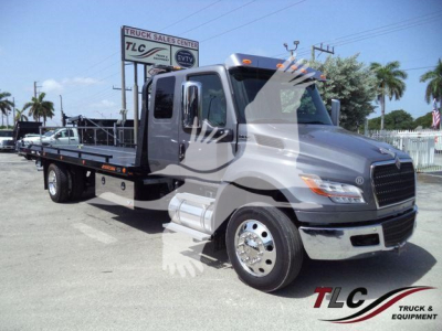 Flatbed tow truck from side/front view with cab and long flat deck, MV model plate visible.