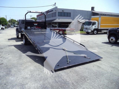 Tow truck rollback flatbed with ramp open, hitching area visible, International MV chassis in background, dealership lot.
