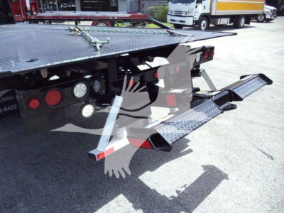 Back of rollback truck showing hydraulic ramps and lights; there are step plates and extension ramps with textured metal surface. Text visible near rear: none legible; general hardware components of tow truck bed.