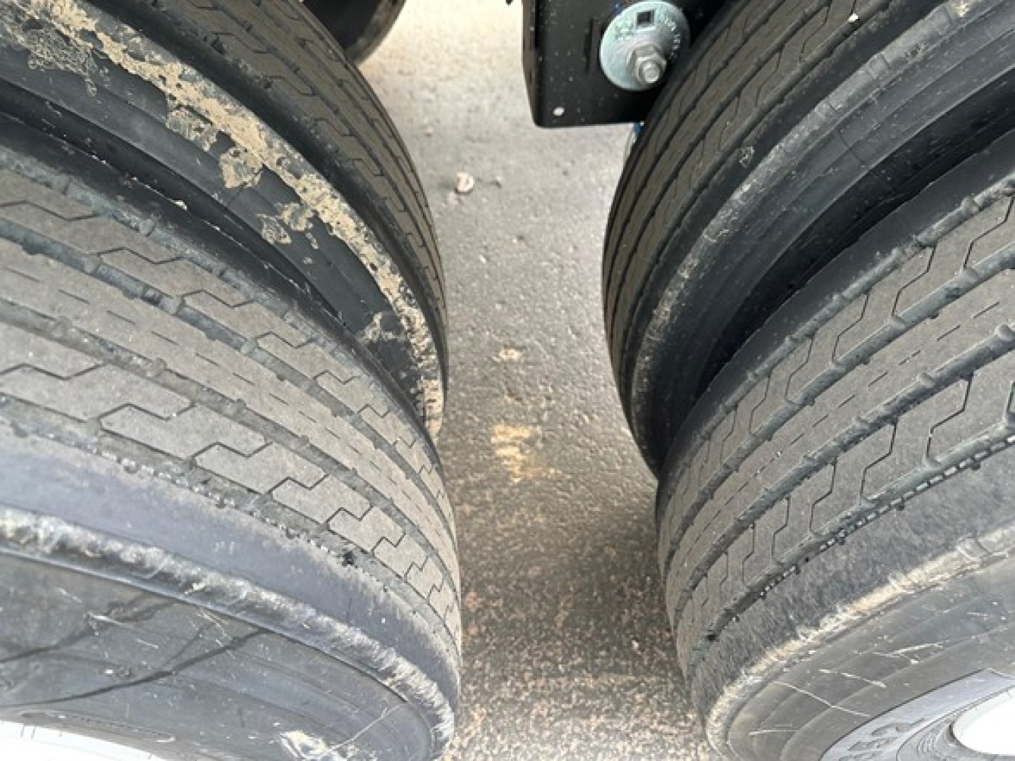 Two large trailer tires viewed from above with a gap between them; dirt and debris on tread; part of axles and undercarriage visible