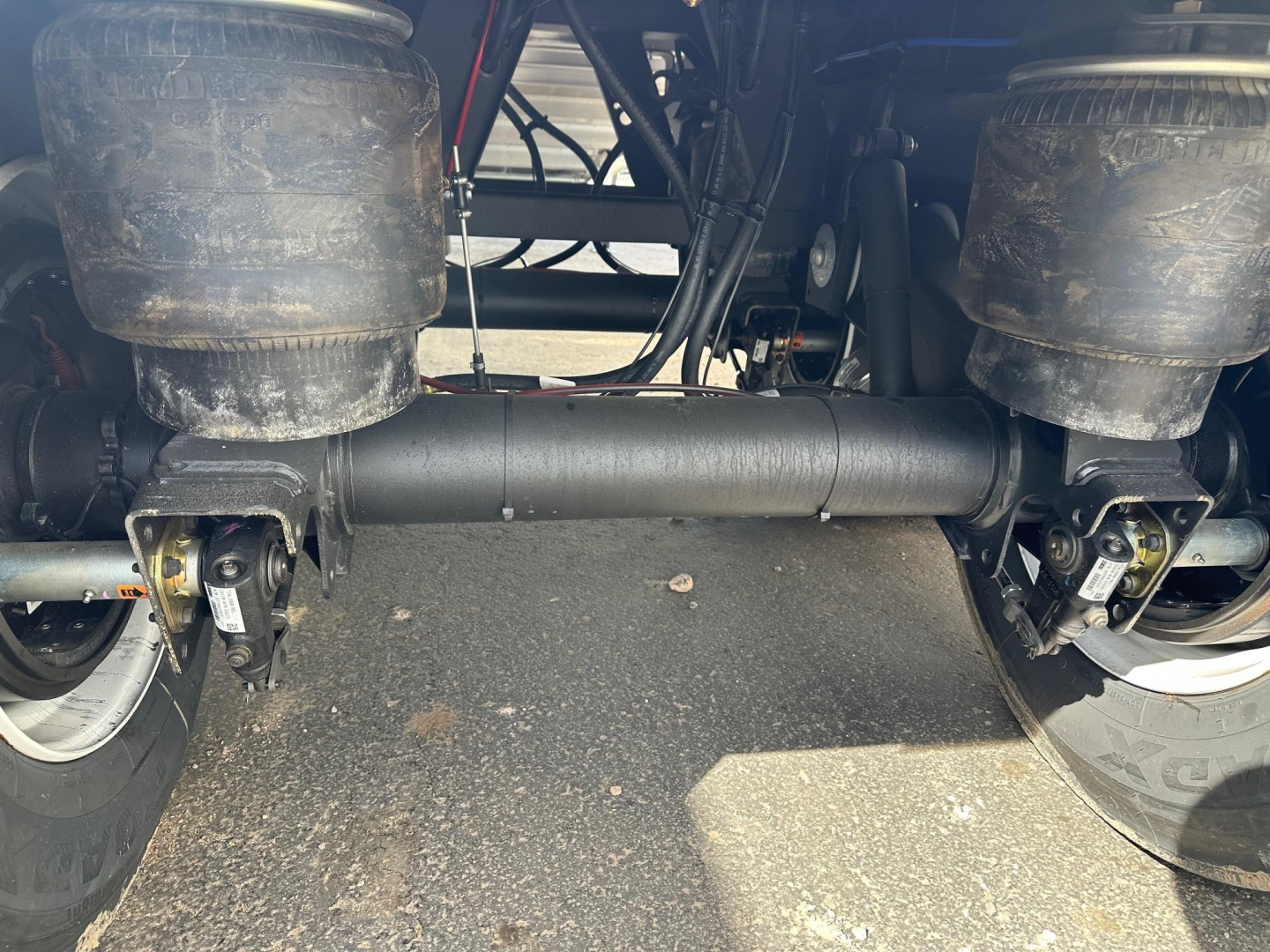 Trailer underside showing suspension and axles with air springs and driveshafts; dual rear wheels; mud and dirt on components.