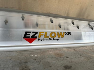 Trailer side showing EZFLOW XR Hydraulic Trap logo on silver metal surface with bolts.