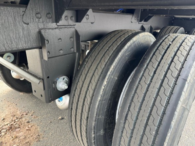 Tandem axle trailer frame and wheels showing suspension and mounting hardware; partial view of dual tires with tread and frame members.