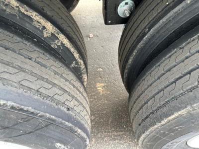 Two large trailer tires viewed from above with a gap between them; dirt and debris on tread; part of axles and undercarriage visible
