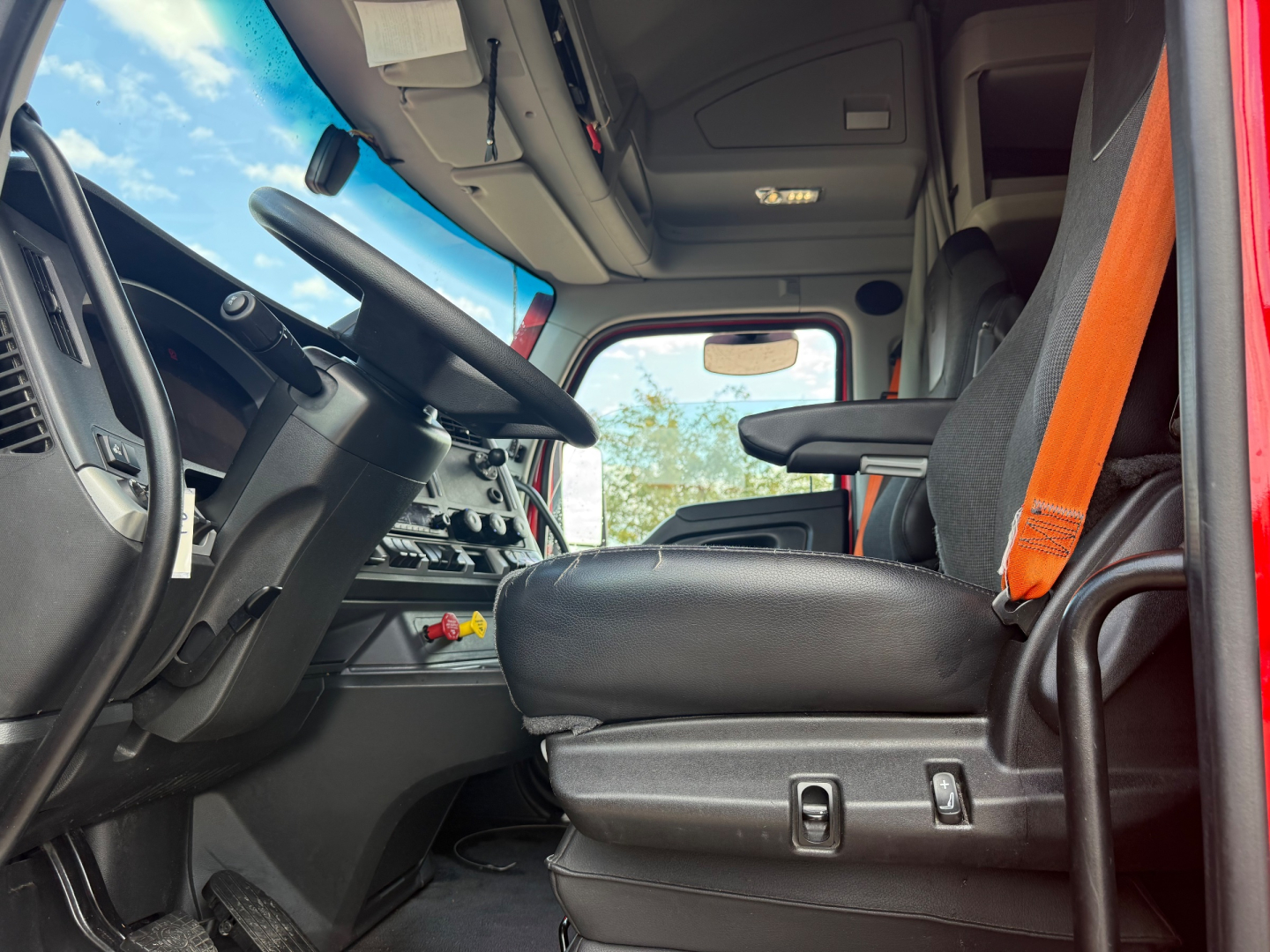 Kenworth T680 cab interior showing driver seat, steering wheel, dashboard controls, and orange seat belt.