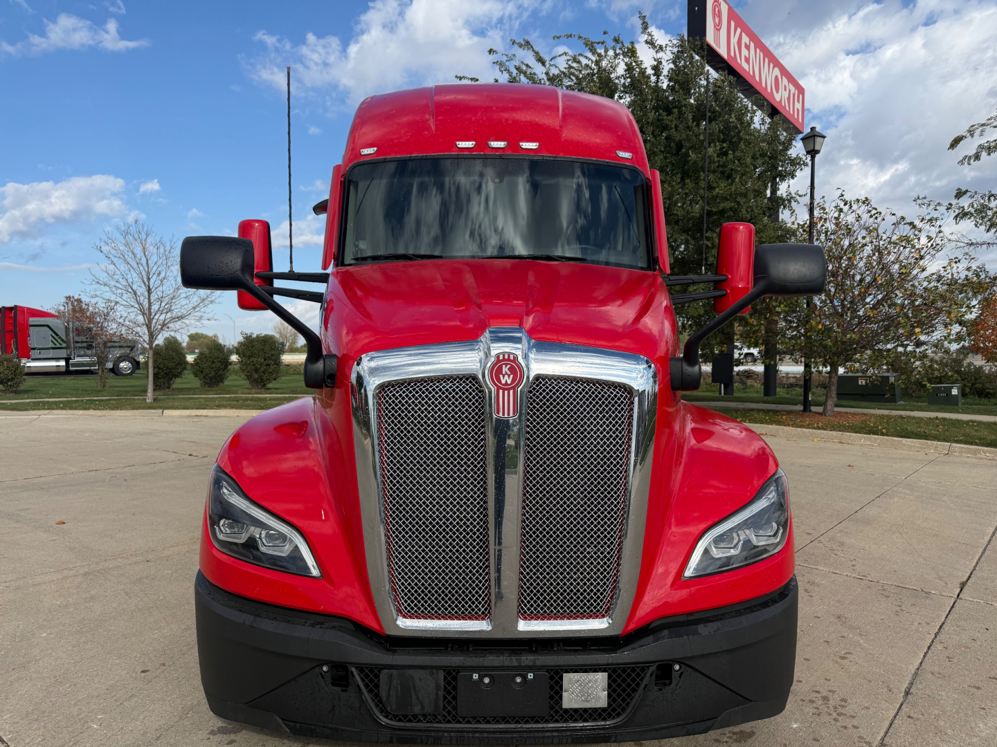 Kenworth T680 truck front view showing bold chrome grille, red cab, black bumper, and side mirrors.