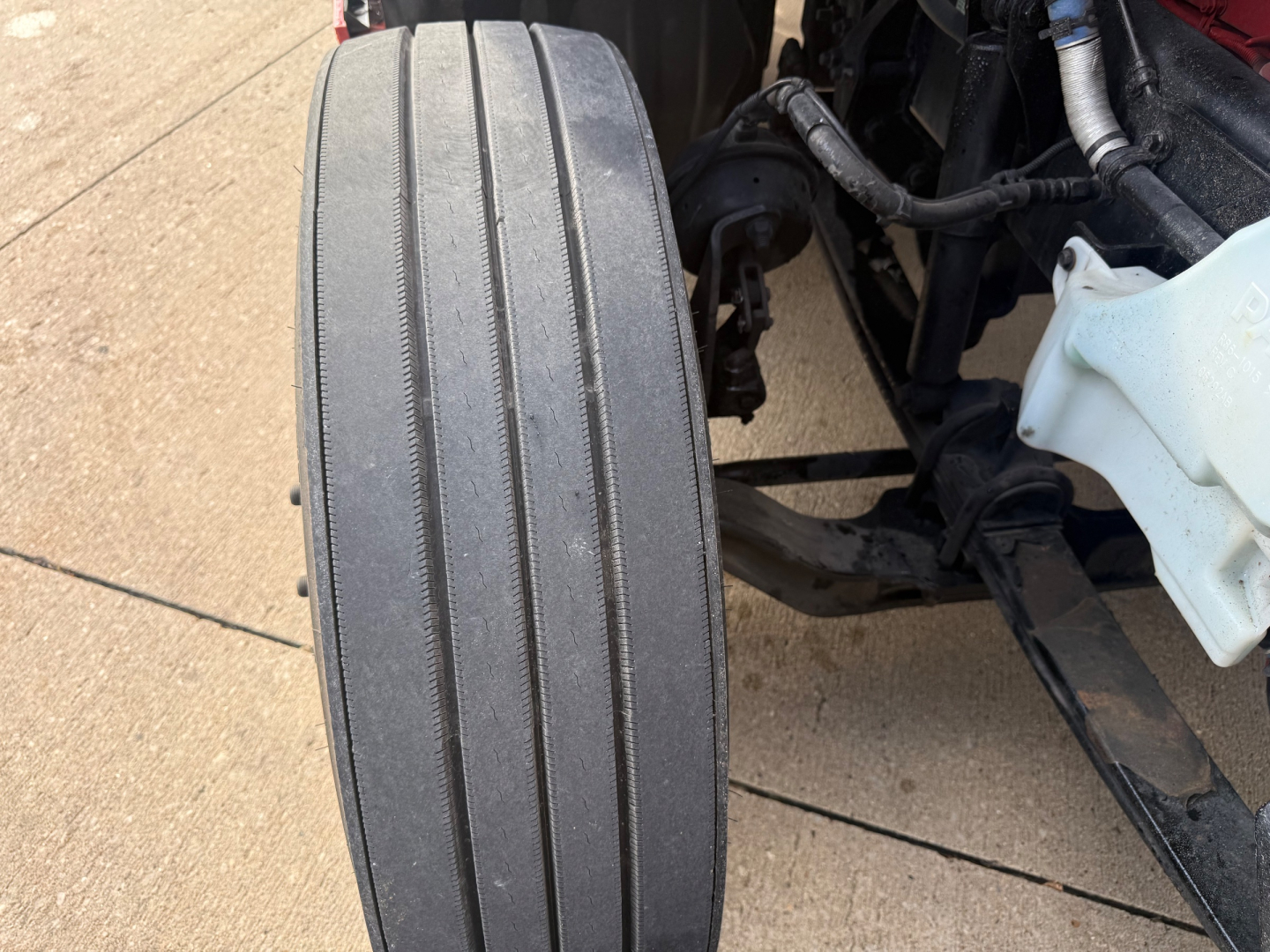 Kenworth T680 front wheel and suspension area with tire tread visible and parts of chassis and coolant reservoir.