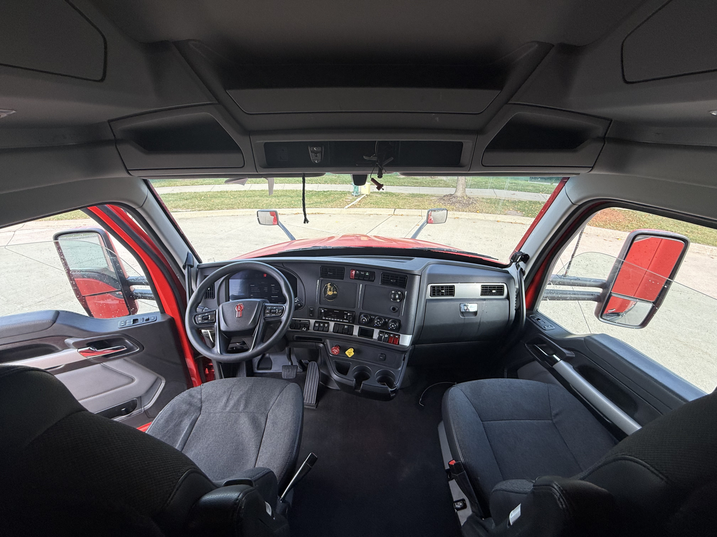 Kenworth T680 truck interior view showing dashboard, steering wheel, drivers and passenger seats, center console, and large windshield.