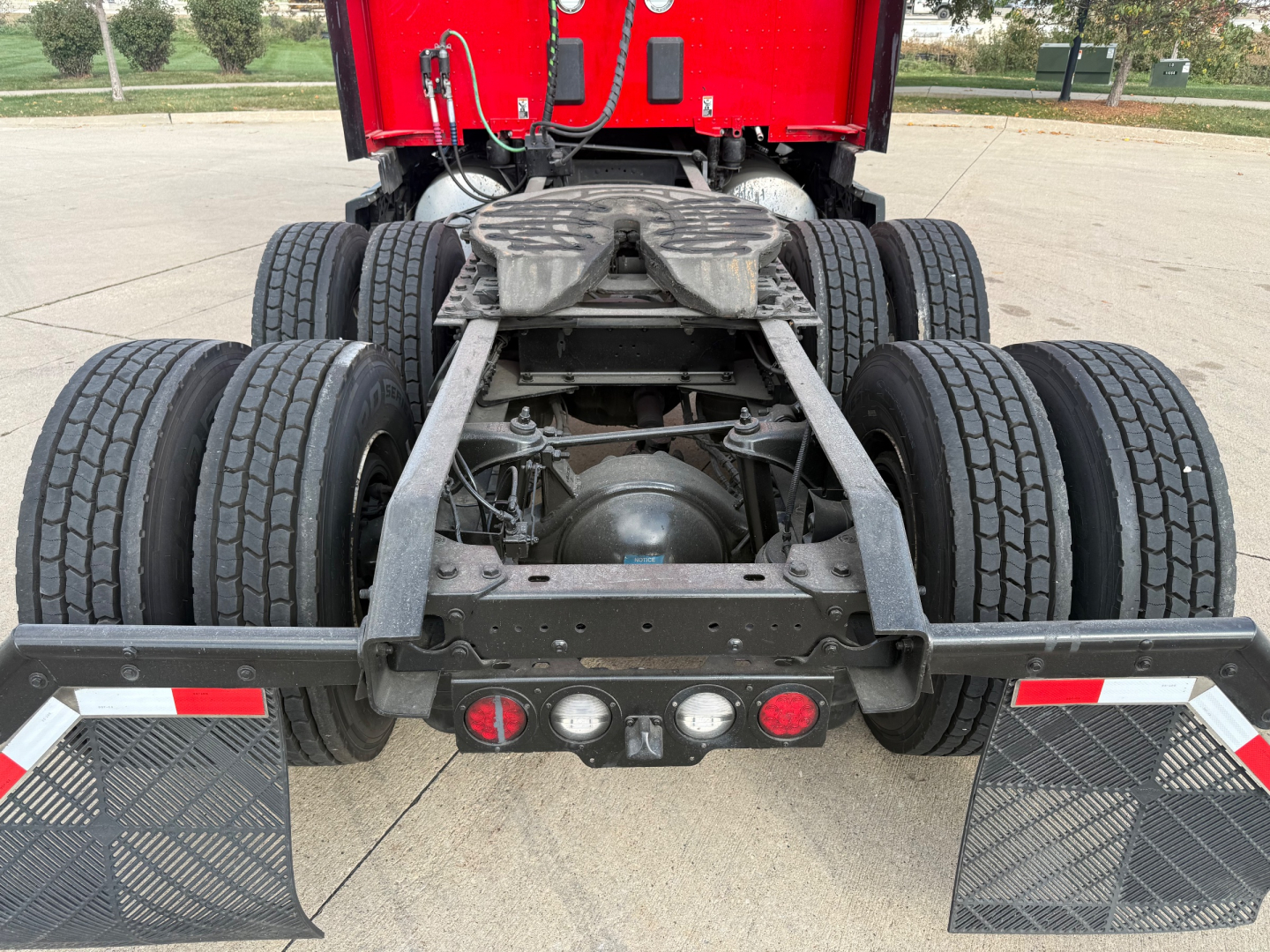 Rear view of a Kenworth T680 tractor chassis showing dual rear axles, fifth wheel, and mud flaps with reflective strips.