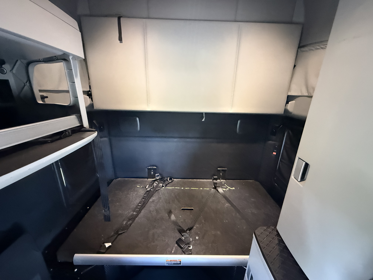 Kenworth T680 sleeper cab interior cargo area showing open storage and metallic floor panel with tie-downs.