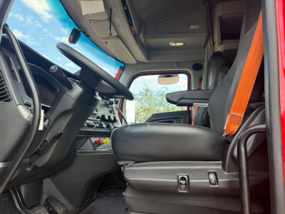 Kenworth T680 cab interior showing driver seat, steering wheel, dashboard controls, and orange seat belt.