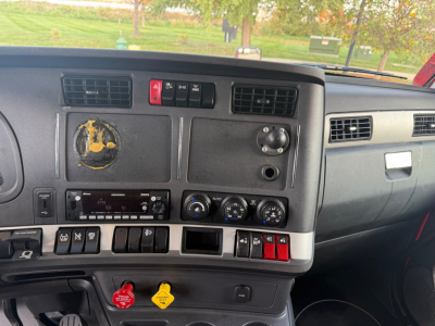Kenworth T680 dashboard with center console including hazard switch, climate controls, and various switches; partial steering wheel area visible; stock/ID details not on panel.