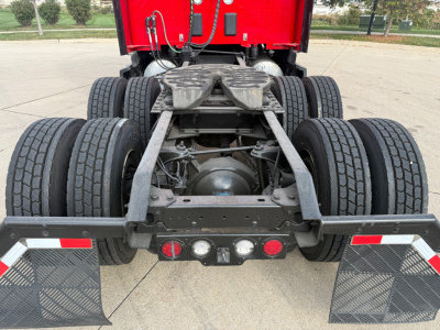 Rear view of a Kenworth T680 tractor chassis showing dual rear axles, fifth wheel, and mud flaps with reflective strips.