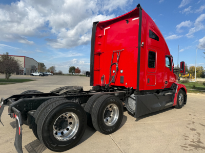 Kenworth T680 sleeper tractor in red, side view showing rear wheels and cab from left rear, with fifth wheel and chassis visible.