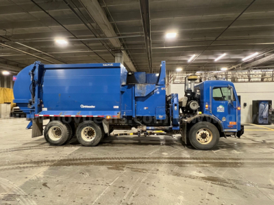 Peterbilt garbage truck side view with blue cab and compactor body, showing Fleet/Brand markings and no visible labels legible from distance.