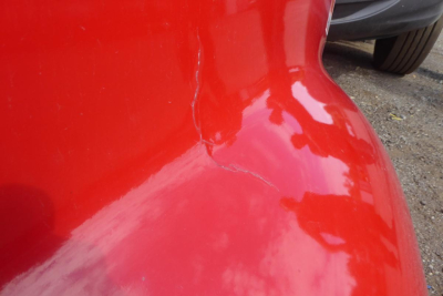 Red exterior of a truck showing a vertical seam/gap near the cab corner and a portion of a tire in the background.
