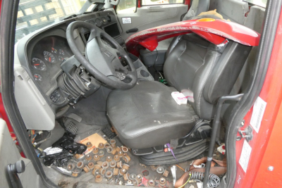 Interior of a 2012 International PROSTAR cab showing steering wheel, dashboard, worn driver's seat, scattered parts on the floor, and exposed wiring.