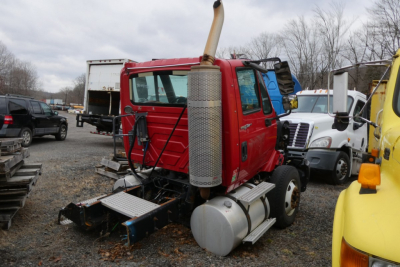 2012 International Prostar conventional daycab truck rear/side view with red cab, large cylindrical exhaust stack, and fuel tanks. Visible text on truck panels not legible.