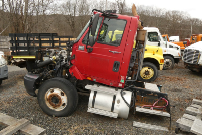 International ProStar conventional day cab truck in yard showing engine bay side view with red cab and fuel tank.