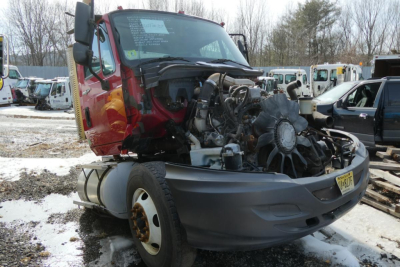 Truck engine exposed in front of a red International ProStar cab with damaged front end, showing radiator, belts, and exposed engine components.