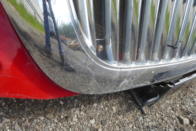 Truck front bumper and grille area of a 2012 International PROSTAR, chrome grille, red fender, black hitch, parked on gravel.