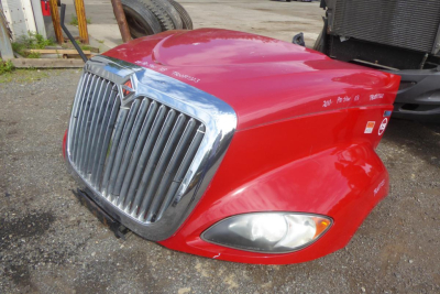 Front-left view of a red International ProStar cab front with chrome grille, headlight, and hood curvature.