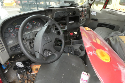 Interior of 2012 International PROSTAR cab showing steering wheel dash gauges and exposed dashboard with red hood nearby.