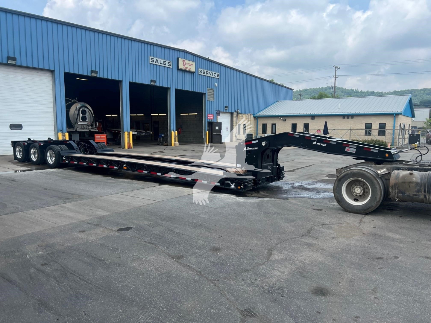 XL Specialized XL110HDGS lowboy trailer in service bay showing long flatbed and hitch with blue industrial building in background.
