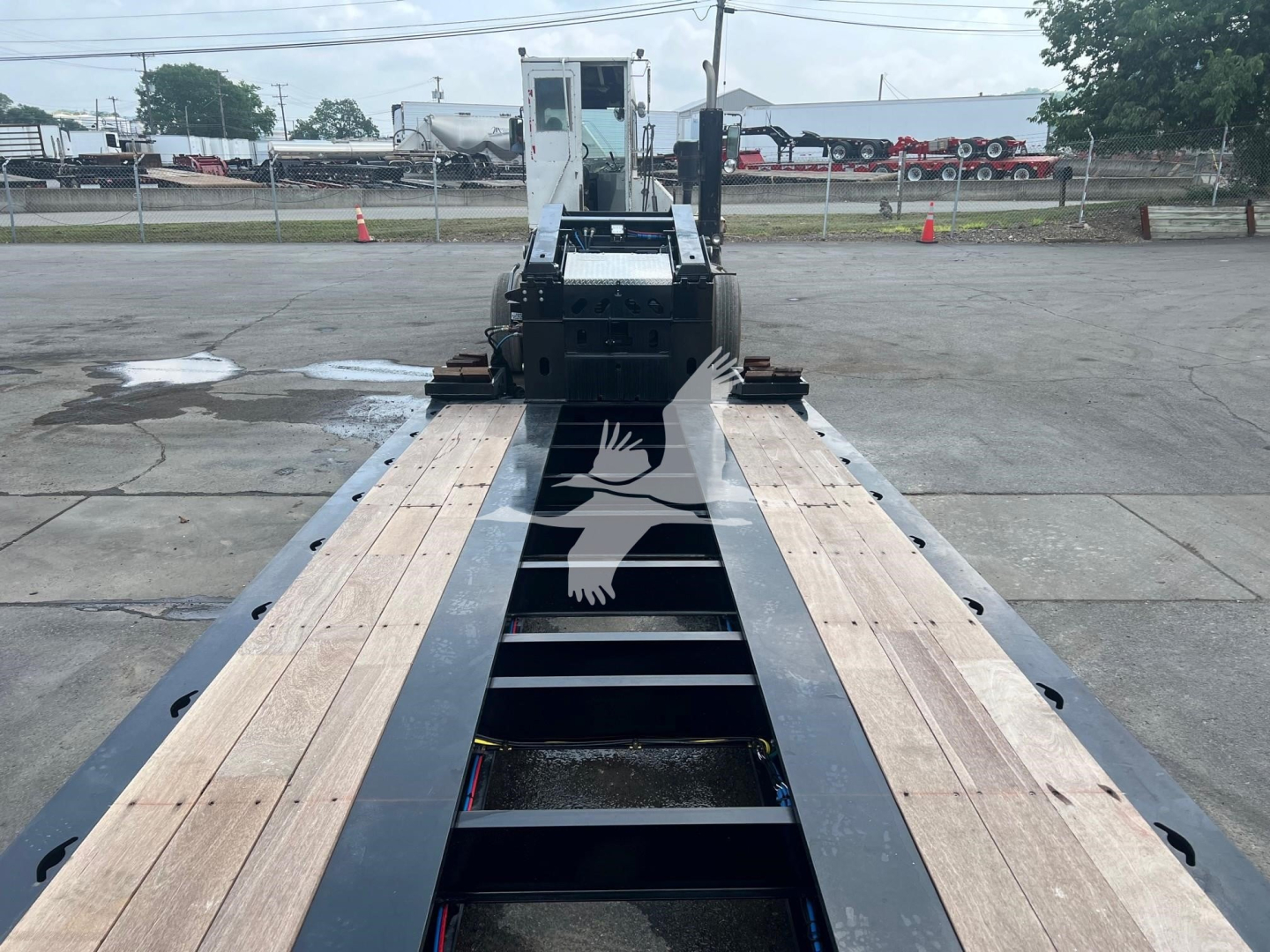 Trailer deck view of a XL Specialized XL110Hdgs lowboy trailer showing wooden deck sections and black steel frame with gooseneck at far end.