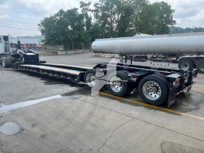 XL Specialized XL110HDGS lowboy trailer showing triple axle configuration and a cylindrical tank on top, side view with wheel rims and deck rails.