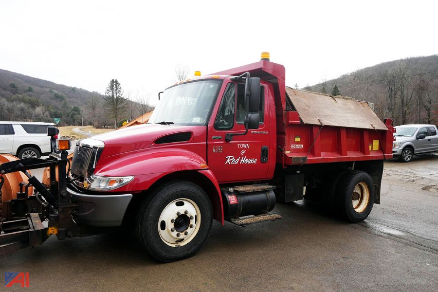 Truck showing red 2004 International 4200 dump bed with plow and spreader in front view.