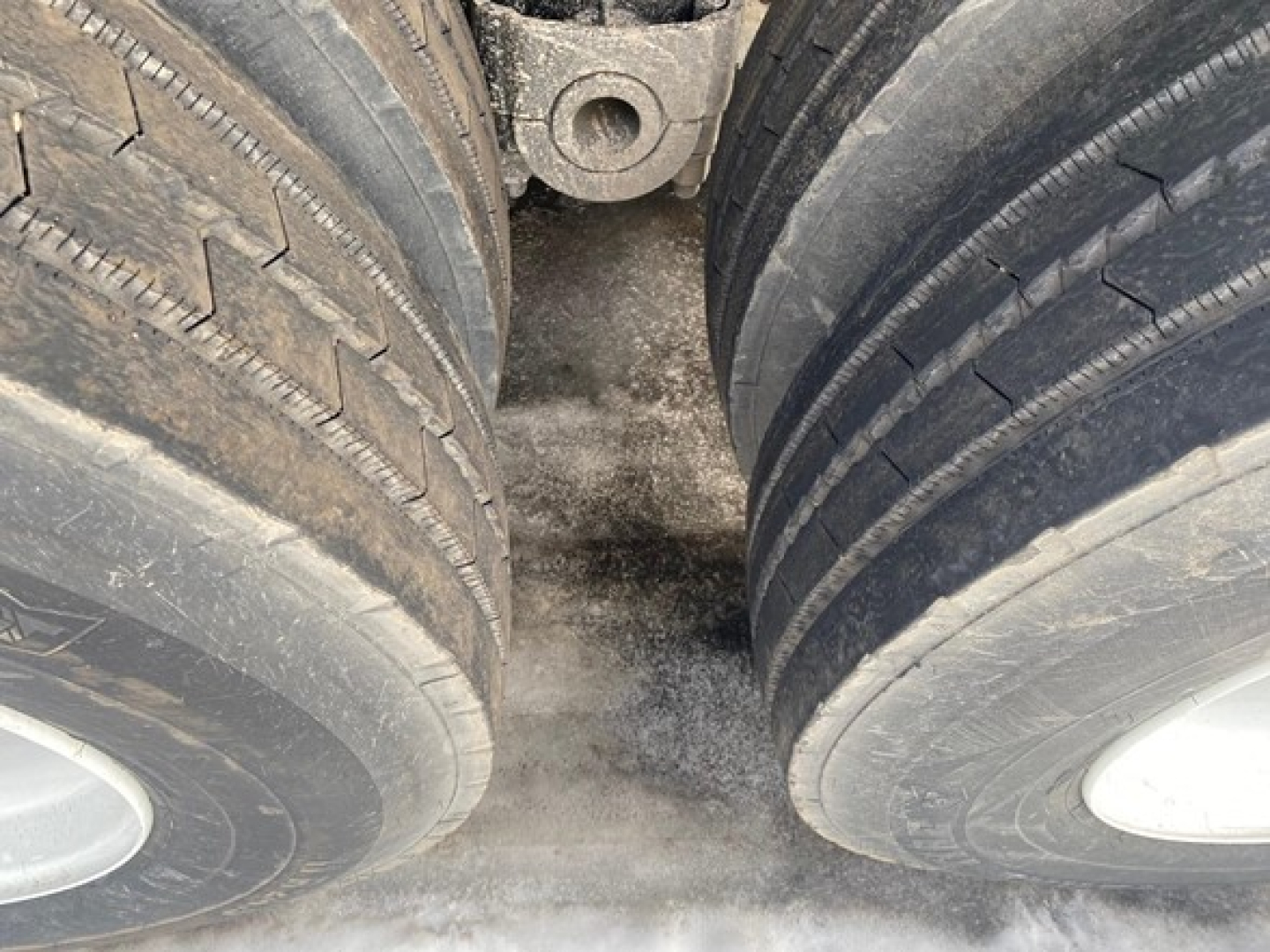 Trailer dual rear axles with tires, view between wheels showing mud and ground; part of a 2024 Mac High Cube 76" Side Scrap Trailer in new condition.