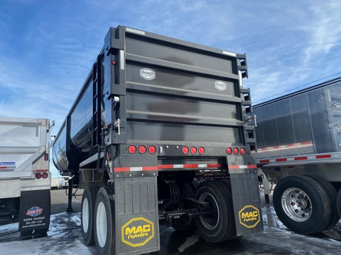 Dakota style dump trailer rear view showing dual tandem wheels, MAC Trailer mud flaps, and black steel walls with red reflective tape.