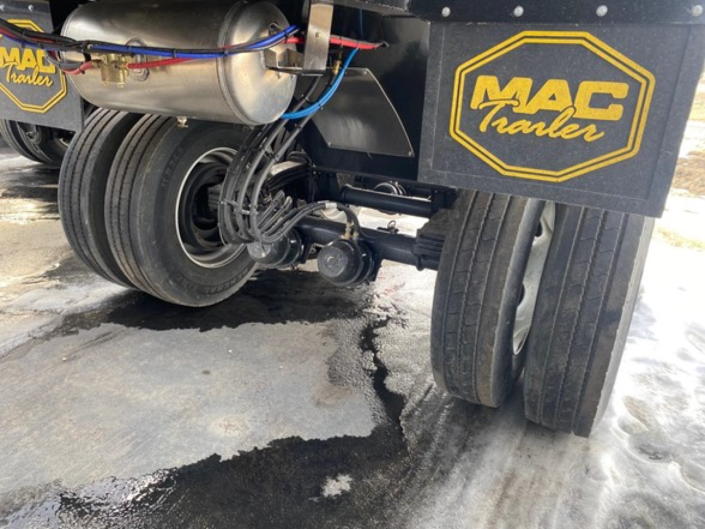 Mac Trailers showing dual rear wheels, suspension, and MAC Traler logo plate. Visible components include air lines, hoses, and a metallic tank.