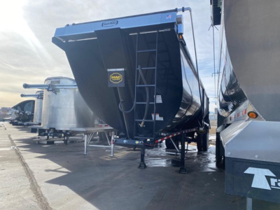 Trailer side scrap dumper showing Mac branding, side-door and ladder, black tote with MAC sticker, blue trailer body, in a lot with other equipment.