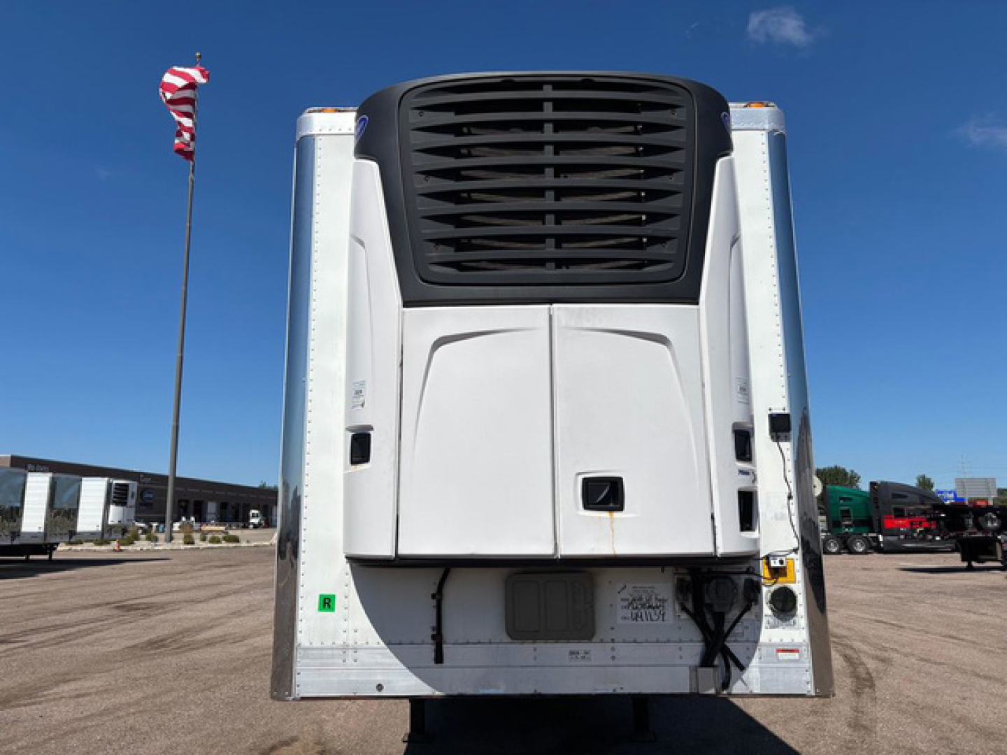 Reefer trailer rear view showing large black radiator/grille and white rear doors with bumper, side frames, and a small green sticker.