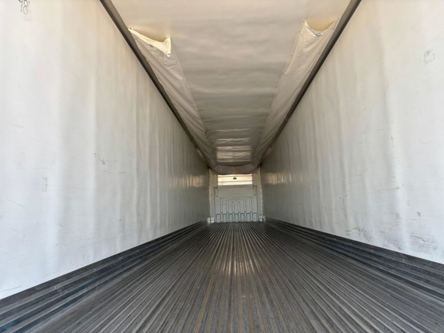 Trailer interior view with white side walls, ribbed floor, narrow cargo area, and rear door opening seen at far end.
